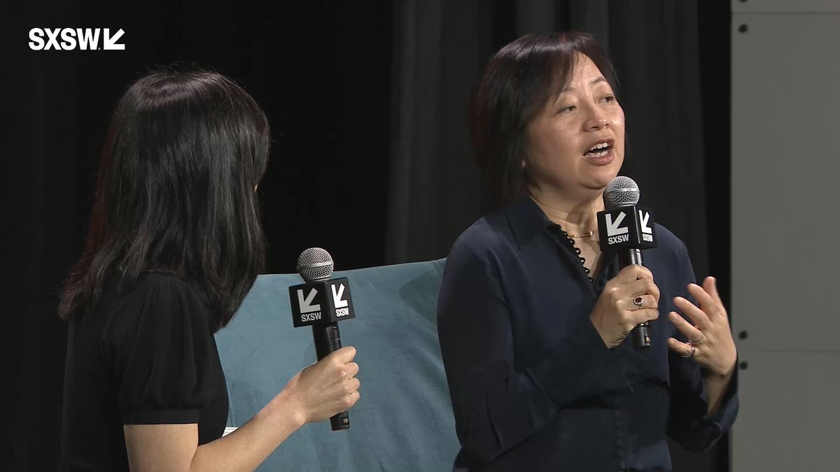 The image shows two women standing next to each other with microphones, both holding them up as they speak into them. The background appears to be a stage or performance area, which suggests that this could be an event where they are discussing the concept of digital currency or sharing their experiences related to it.