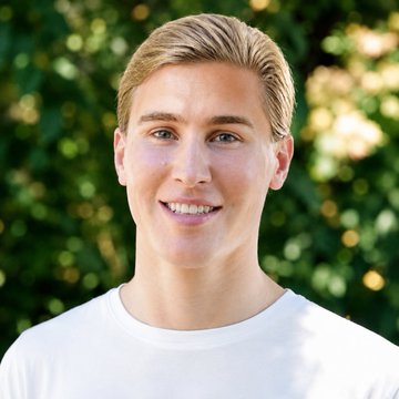A young man with blond hair and a bright smile poses outdoors in a white t-shirt, his polished appearance reflecting the post's claim of having spent €40k on plastic surgery to resemble influencer Joe Nakamoto.