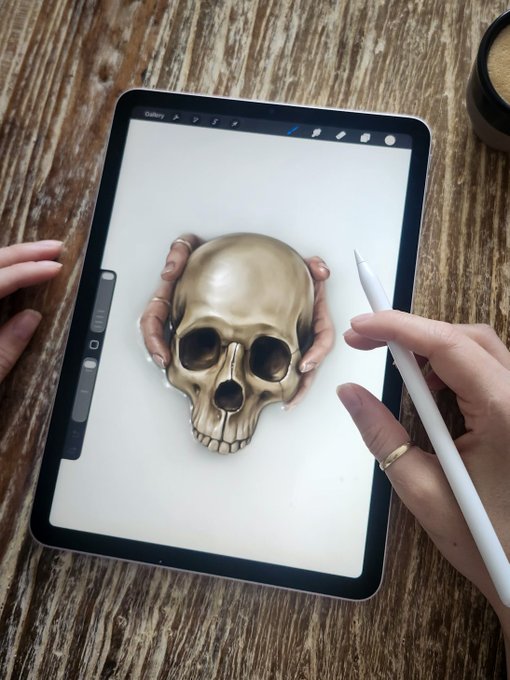 A digital artist working on an iPad with a stylus, drawing a realistic image of hands holding a skull.
