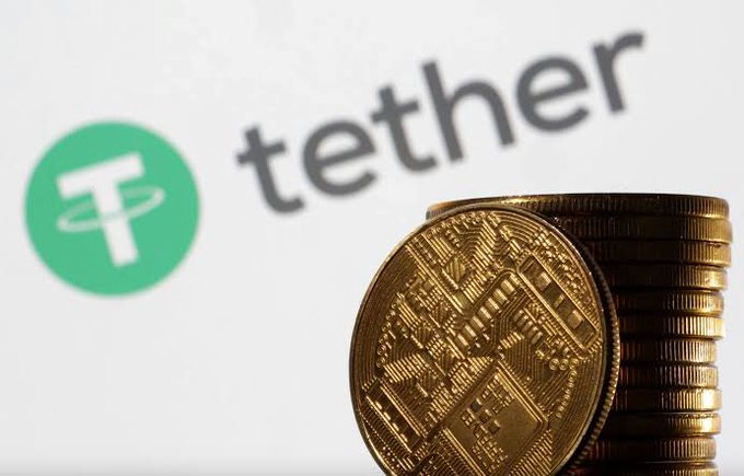 A photograph showing the Tether (USDT) logo in the background with a stack of gold physical cryptocurrency coins in the foreground.