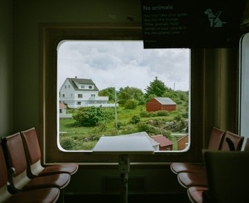 A view through a train window showing houses and greenery outside, with red seats visible inside and a sign reading 'No animals' near the window.