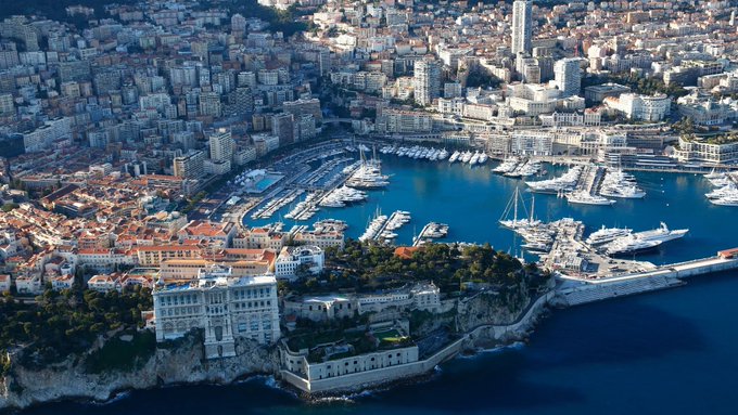 The image depicts a cityscape with boats in a large harbor, surrounded by mountainside buildings. There are several tall buildings lining the edges of the city along the coast. The scene is an aerial view showing the vast expanse of the ocean where numerous boats can be seen floating on its surface near the shoreline. The post also mentions Bitcoin and cryptocurrency as tax-free income in the state, which adds to the attractiveness of this location for high net worth individuals looking to invest or establish their residence.