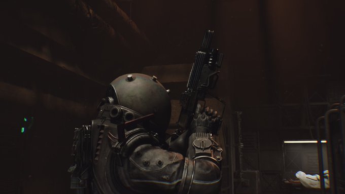 A dark, atmospheric video game scene shows a character in a metallic helmet and armor holding a rifle in a dimly lit industrial setting.