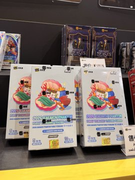 Three identical Pudgy Penguins x Kakao Friends collectible card boxes are displayed on a shelf, featuring artwork of a chubby penguin with pink hair holding a green book, priced at $19.99 each. The packaging also references a collaboration with the game Genshin Impact, confirming the post's excitement about seeing Pudgy Penguins merchandise alongside the Genshin logo at the Shanghai Kakao Carnival.
