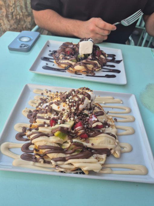 Two plates of indulgent desserts topped with cream, chocolate sauce, and colorful sprinkles served on a light blue table.