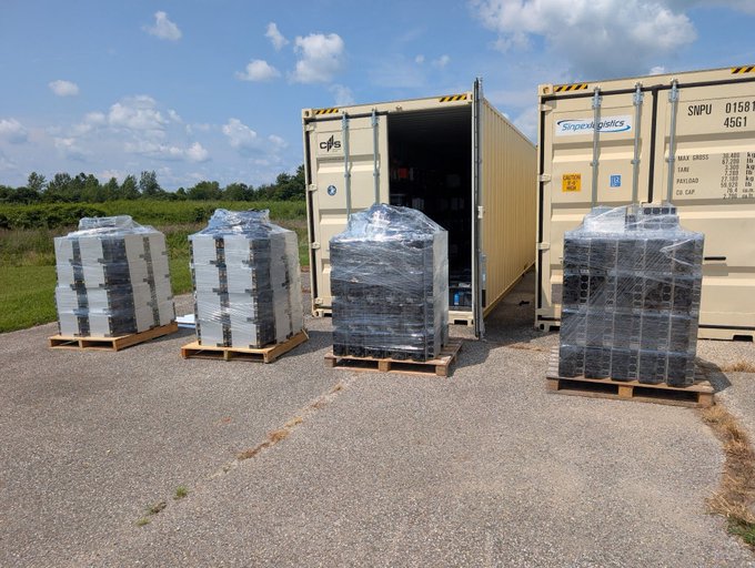 Four pallets of shrink-wrapped industrial components sit in front of an open shipping container labeled 'SNPU 0158 45G1' with 'Snipes Logistics' branding in an outdoor lot.