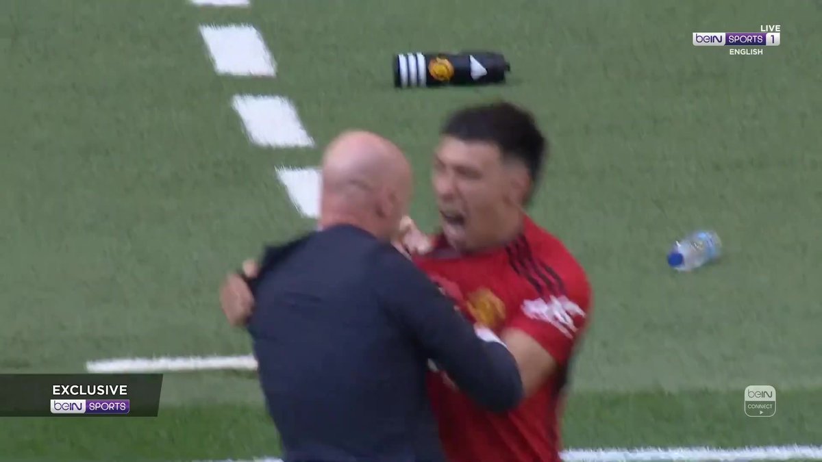 A jubilant Manchester United player in a red jersey embraces manager Erik ten Hag on the pitch during a live beIN Sports 1 broadcast, capturing an emotional celebratory moment likely following a significant victory.