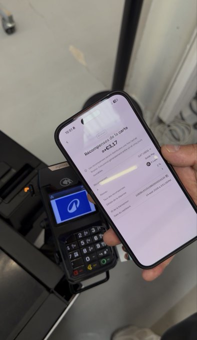 A hand holds a smartphone displaying an OKX app screen showing a €43.17 cashback reward from a "Riconoscimento" (recognition/reward), while in the background another person holds an Ingenico payment terminal at a checkout, visually confirming the recent purchase that triggered the 2% minimum cashback return mentioned in the post.