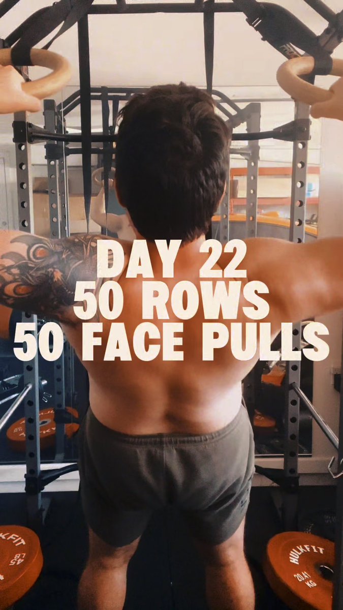 A shirtless man with a tattooed arm uses gym rings for an exercise, with overlaid text reading 'DAY 22, 50 ROWS, 50 FACE PULLS'.