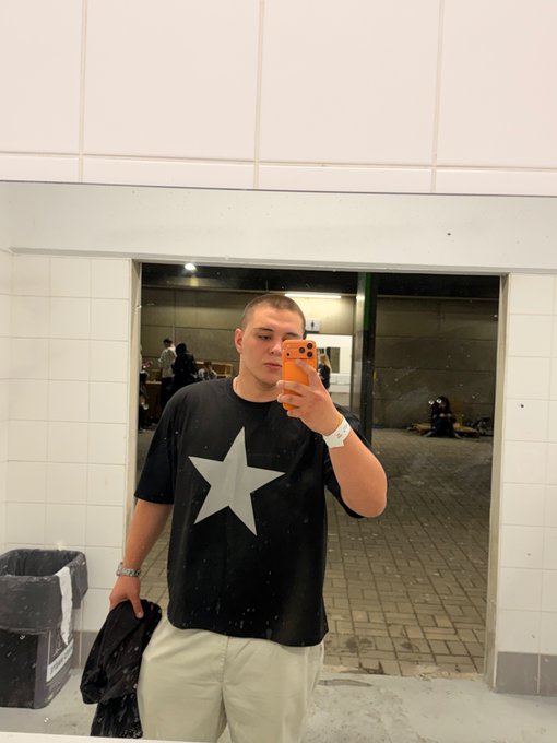 A man taking a selfie with his cell phone, wearing a black t-shirt that has "a star" printed on it.