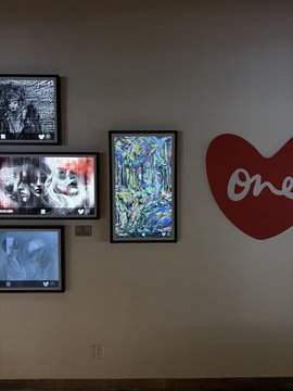 Art gallery display showing framed artworks alongside a large red heart sculpture with 'One' written on it.