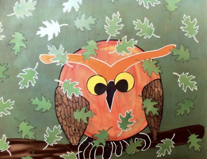 A whimsical painting shows an orange and brown owl with large yellow eyes perched on a branch against a green background scattered with green leaves.