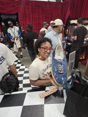 A woman proudly holds up a pair of black-and-white checkered Vans sneakers featuring "Satoshi Nakamoto" branding at ComplexCon, showcasing the highly sought-after collaboration.