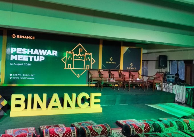 An indoor event space set up for a 'BINANCE PESHAWAR MEETUP' on '13 August 2026' from '5:30 PM - 9:30 PM PKT' at 'Serena Hotel Peshawar', with a green color scheme and decorative floor cushions.