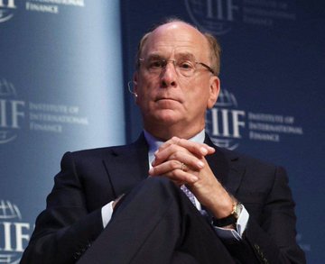 An older man with glasses in a dark suit sits with hands clasped against a backdrop featuring the 'IIF' (Institute of International Finance) logo.