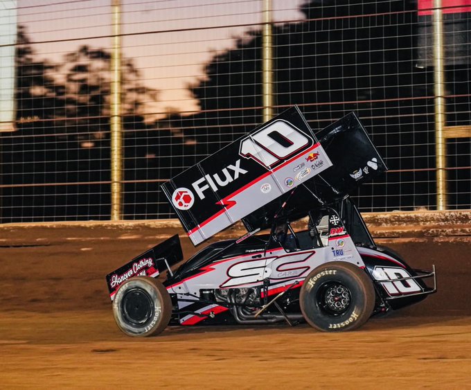 A black, white, and red sprint car numbered 10 with 'Flux' and 'SC' branding racing on a dirt track at sunset.