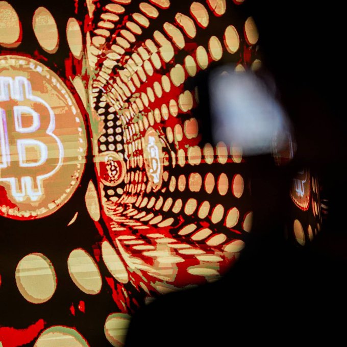 A man gazes at an immersive digital display of glowing Bitcoin logos and symbols in red and orange tones, reflecting the thrill of rediscovering a long-lost fortune in cryptocurrency.