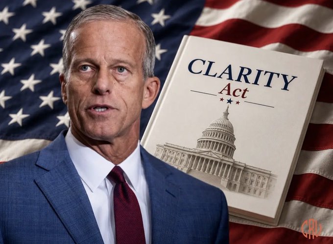 A man in a blue suit and red tie stands beside a graphic of the "CLARITY Act" book featuring the U.S. Capitol dome, with an American flag in the background, illustrating Majority Leader Thune's push to advance the crypto legislation before the August recess.