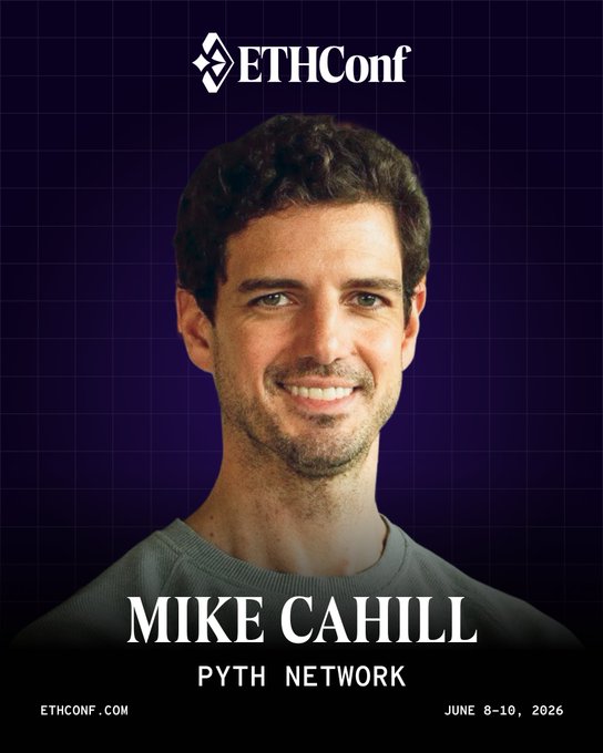 The image features a man with short brown hair wearing a gray shirt, smiling at the camera. The background of the image is purple, which contrasts with the man's light skin tone. The text "Mike Cahill" is written on his shirt in white letters. The image also includes a logo for @mdomcahill and an event name "@ethconf".