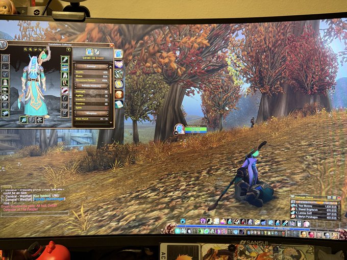 A monitor displays a World of Warcraft gameplay scene in an autumn forest, showing a 'Level 14 Druid' character panel on the left and damage meters at the bottom.
