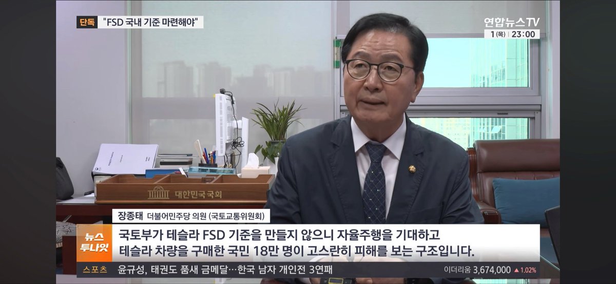 A news broadcast screenshot from 연합뉴스TV showing an interview with 장종태 (국토교통위원회), discussing 'FSD 국내 기준 마련해야' (Need to establish domestic standards for Tesla FSD), with subtitle '국토부가 테슬라 FSD 기준을 만들지 않으니 자율주행을 기대하고 테슬라 차량을 구매한 국민 18만 명이 고소한 피해를 보는 구조입니다.'