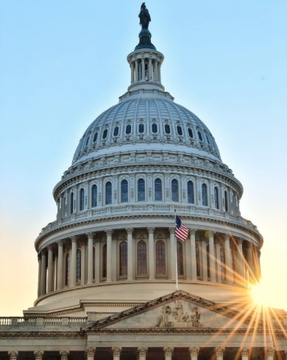 The United States Capitol dome is illuminated against a sunset sky, with the American flag visible on its facade and the sun creating a starburst effect behind the building. The image symbolizes the legislative progress mentioned in the post, representing the U.S. House committees where the Digital Asset Tax Certainty Act and American Reserve Modernization Act recently advanced.