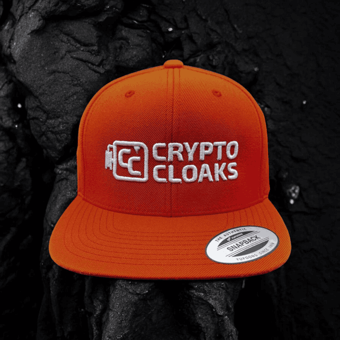 A bright orange snapback hat featuring the embroidered white "CRYPTO CLOAKS" logo is displayed against a dark, textured black background.