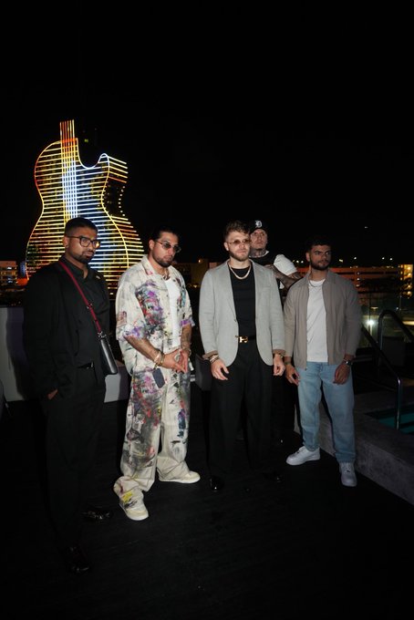 Five men pose together at night outdoors in front of an illuminated guitar-shaped building.