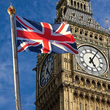 The Union Jack flag waves in the foreground with the iconic Big Ben clock tower, whose face reads approximately 9:17, visible in the background against a clear blue sky. The image underscores the UK context of the news about British lawmakers addressing crypto banking barriers.