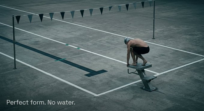 An advertisement-style image of a swimmer in a crouched starting position on a diving block on an empty pool deck, with the caption 'Perfect form. No water.'