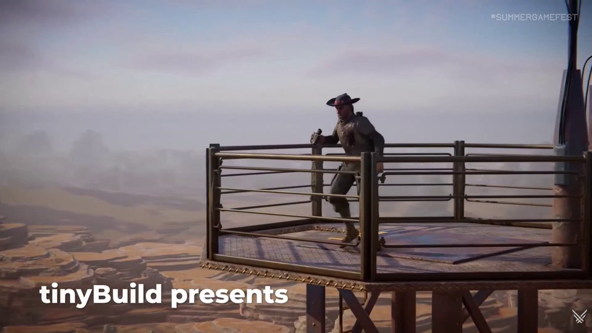 The image shows a person standing on top of a metal structure or platform that has been turned into a fortification. The individual appears to be wearing a hat, possibly a cowboy hat, which adds to the overall theme of the scene. The background features a desert-like setting with sand dunes and mountains in the distance, creating an atmosphere reminiscent of a post-apocalyptic world. The image is related to the post because it showcases a miniature fortification built by someone who has used tinyBuild to create this impressive structure.