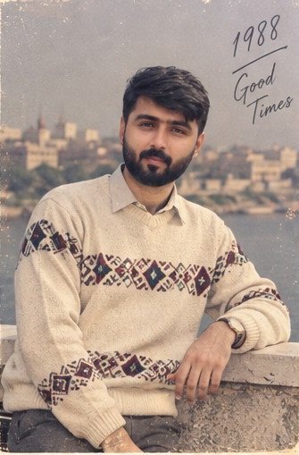 A man with dark hair and a beard wears a cream-colored patterned sweater, photographed against a coastal city backdrop with the text '1988 Good Times' in the upper right corner.