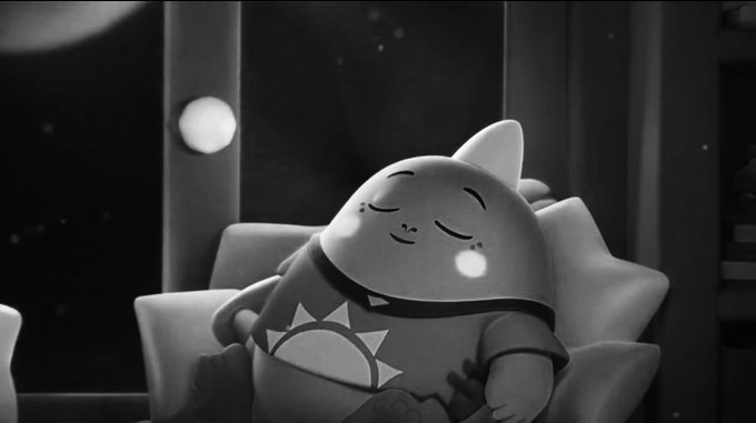 A black and white scene shows a sleeping round character wearing a shirt with a sun design, resting against a pillow with closed eyes.