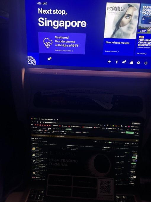 A United Airlines seatback screen displays 'Next stop, Singapore' with the flight number 'UA1' and a weather alert for scattered thunderstorms with highs of 94°F, while a laptop in the foreground shows a trading terminal.