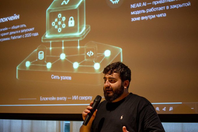 A bearded man speaks into a microphone during a presentation, with a slide behind him displaying a diagram of blockchain nodes ("Сеть узлов") and text about NEAR AI operating in a closed Chinese zone. The image illustrates his talk on NEAR and NEAR AI at the AI Event in Batumi, Georgia.