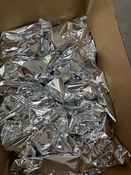 An open cardboard box filled with crumpled, shiny silver packaging material.