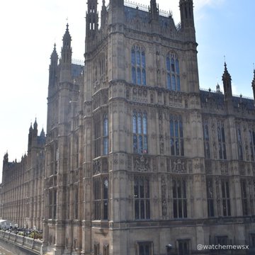 A photograph of the Houses of Parliament in London, showcasing its detailed Gothic architecture against a clear blue sky, with the watermark "@watchemewsx" visible in the corner.