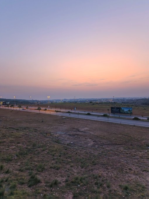 A vast empty field at sunset, with a billboard visible in the distance, visually embodies the "touching grass" sentiment of stepping away from the screen and embracing the quiet stillness of real life.