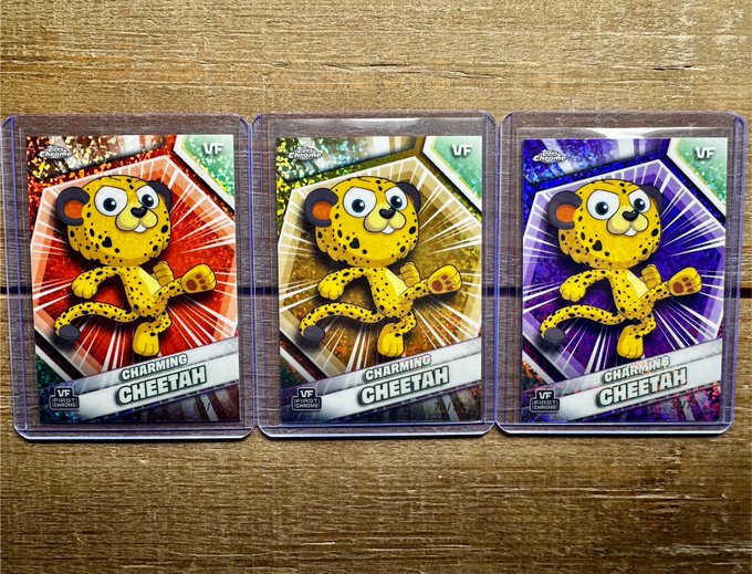 Three Pokemon trading cards featuring 'Charming Cheetah' cards with red, gold, and purple holographic backgrounds rest on a wooden surface.