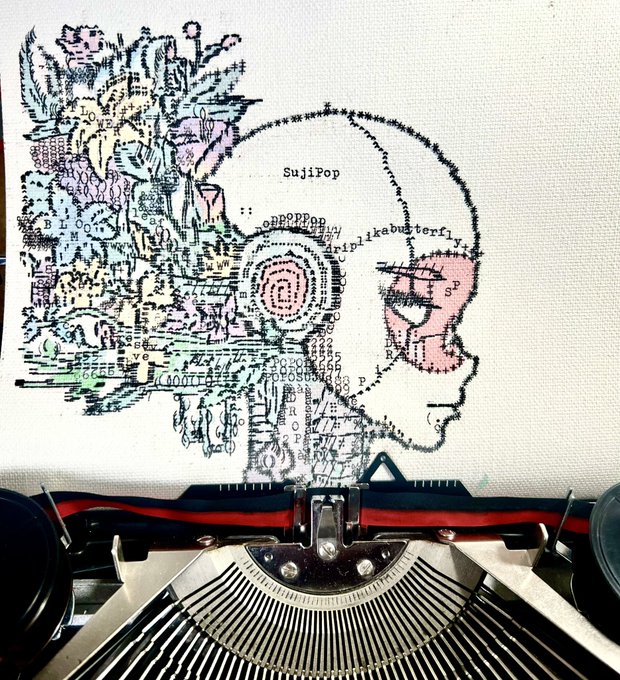 A typewriter with red and black ribbon rests below a piece of paper featuring a complex, abstract cross-stitched pattern that incorporates text like 'SujiPop' and 'purplebutterfly'.
