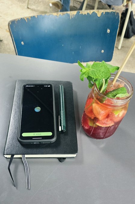 A smartphone displaying the Jupiter app's "All synced" screen rests on a black notebook beside a refreshing glass of berry mojito garnished with fresh mint, embodying the post's message of taking a shaded break to effortlessly complete to-do list tasks. The scene captures the perfect balance of productivity and relaxation that the app promises.