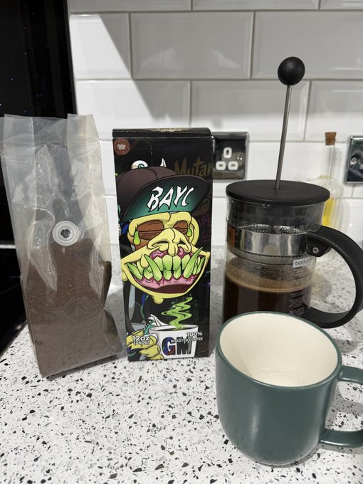 Kitchen counter scene with a French press coffee maker, a green mug, a bag of dark ground coffee, and a box of 'Mutant' brand mushrooms featuring a green skull mascot graphic.