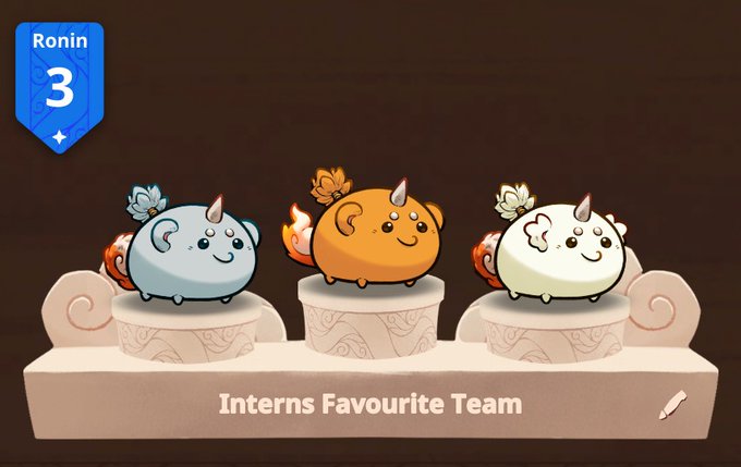 Three adorable round Axies (a blue, an orange, and a cream-colored one), each wearing a decorative flower and a small horn, stand atop podium-like pedestals labeled "Interns Favourite Team," with a "Ronin 3" badge displayed in the upper left corner. The image directly illustrates the post's call to showcase a trio of axies, presenting an example of a charming three-axie lineup.