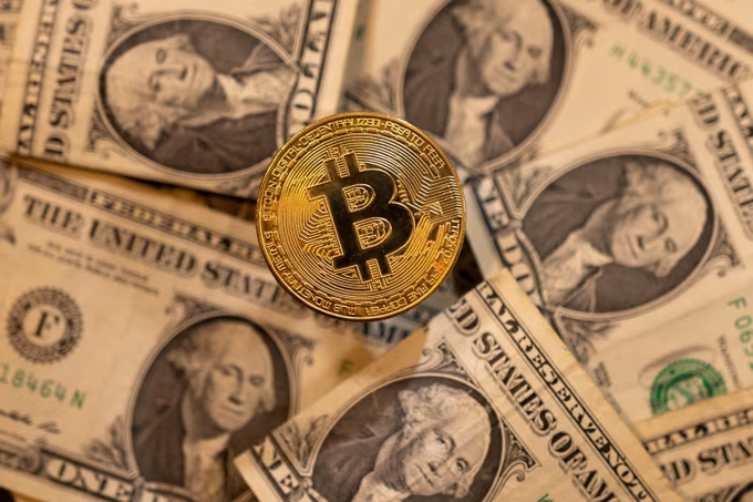A physical Bitcoin token rests on a bed of US one-dollar bills featuring George Washington.