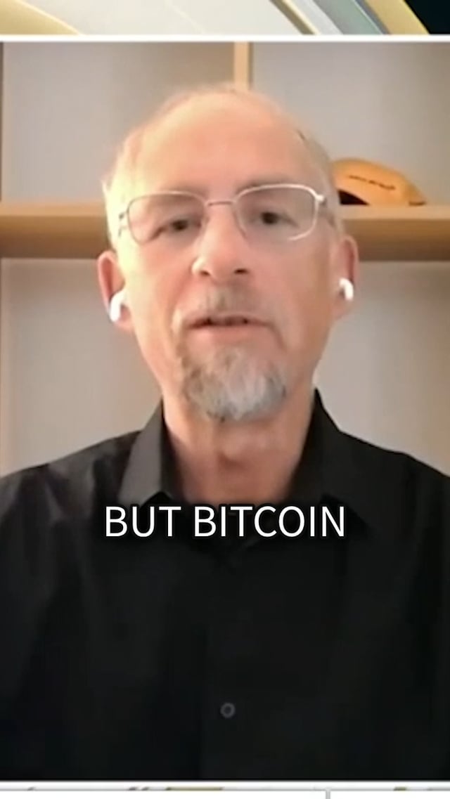 The image shows a man wearing glasses, sitting at a desk or table while talking into a microphone. The background features a bookshelf filled with various items such as books and a cup. The caption of the image reads "No, it' s not me." This suggests that the image is related to a discussion about Bitcoin, which has been circulating on social media platforms like Facebook.