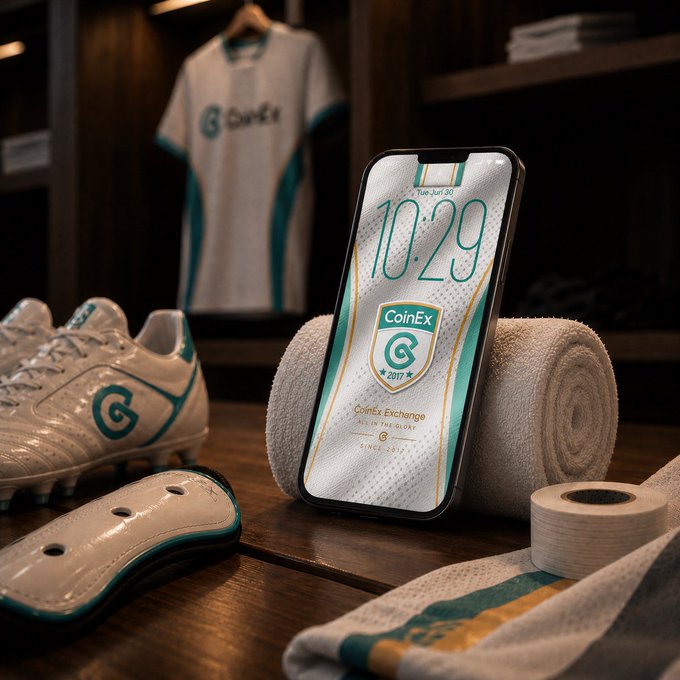 A smartphone propped on a rolled white towel displays a "CoinEx" lock screen showing "10:29," alongside football cleats, a shin guard, and a jersey with a "G" logo in a locker room setting — visually capturing the "Ready before the whistle" pre-game preparation moment.