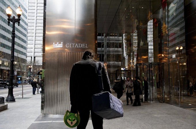 A businessman carrying a duffel bag and a Wolf-themed shopping bag enters the Citadel building in an urban setting. The wolf imagery ties into the post's "WOOF PACK" theme, symbolizing the rallying of wolf-like traders at Citadel—a well-known hedge fund—while the Robinhood Crypto reference highlights the Robinhood connection with the wolf symbolism.