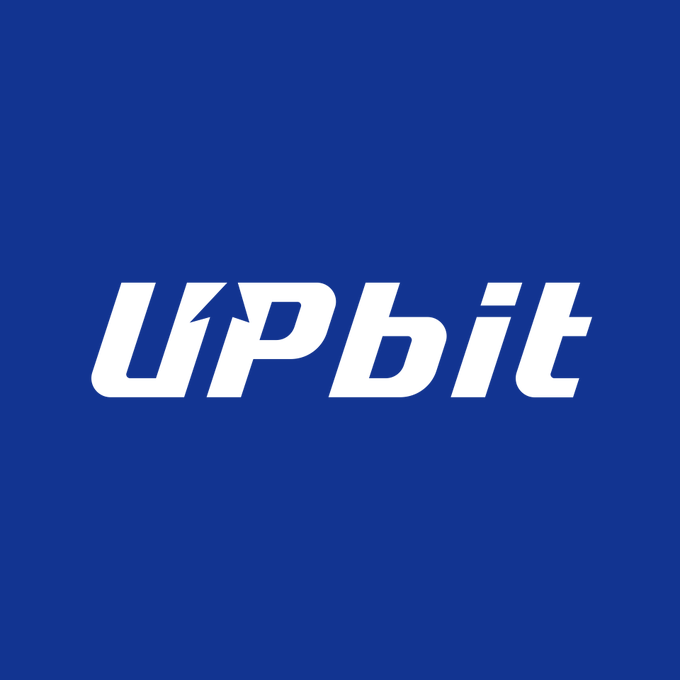 The image displays the white "UPbit" logo in bold, slanted lettering with a small upward arrow inside the "U," set against a solid blue background. The logo corresponds to Upbit, the South Korean cryptocurrency exchange whose parent company Dunamu reported a sharp 49.1% decline in H1 operating revenue amid a contracting global digital asset market.