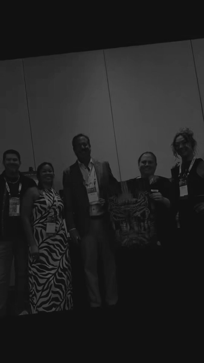 The image features a group of five people standing together, posing for a photo with smiles on their faces. They are all wearing business attire, which suggests that they might be attending an event or gathering related to cryptocurrency or blockchain technology. The background is plain white, providing a neutral backdrop that allows the focus to remain on the group and their expressions.