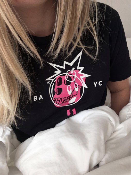 The image features a person wearing a black t-shirt with a graphic design of a skull and crossbones, along with the text "B @B @C". The person appears to be sitting or lying down while wearing this shirt. The post in question asks if it is okay to sleep in the @BoredApeYC merch. This suggests that the image might have been taken at a store where the t-shirt was being sold, and the person has decided to try on the shirt before purchasing it.
